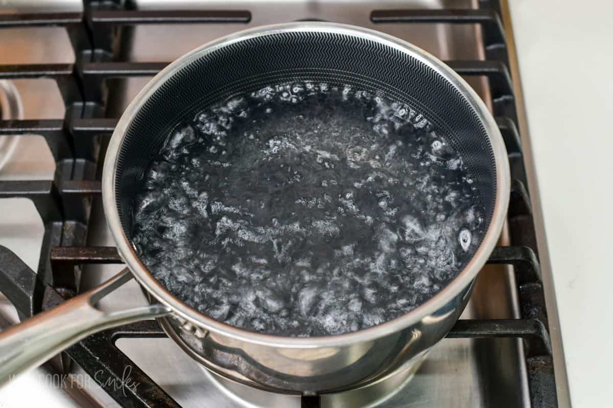 Saucepan of water at a rolling boil on a stovetop, ready for cooking eggs.
