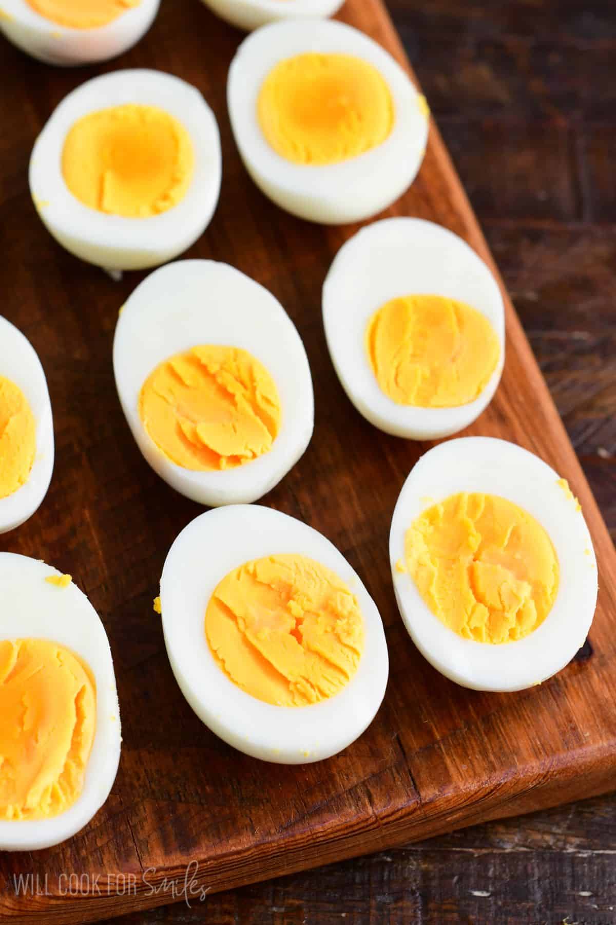 Halved hard-boiled eggs arranged on a wooden cutting board, showing firm egg whites and bright yellow yolks.
