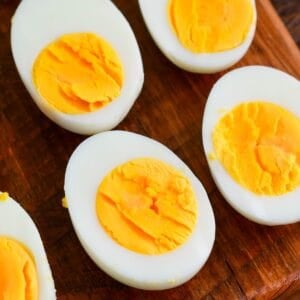 Close-up of halved hard-boiled eggs on a wooden cutting board, showing smooth whites and firm yellow yolks.