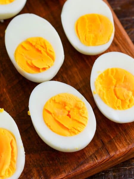 Close-up of halved hard-boiled eggs on a wooden cutting board, showing smooth whites and firm yellow yolks.