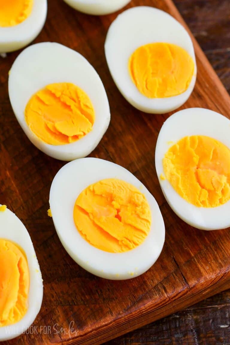 Close-up of halved hard-boiled eggs on a wooden cutting board, showing smooth whites and firm yellow yolks.