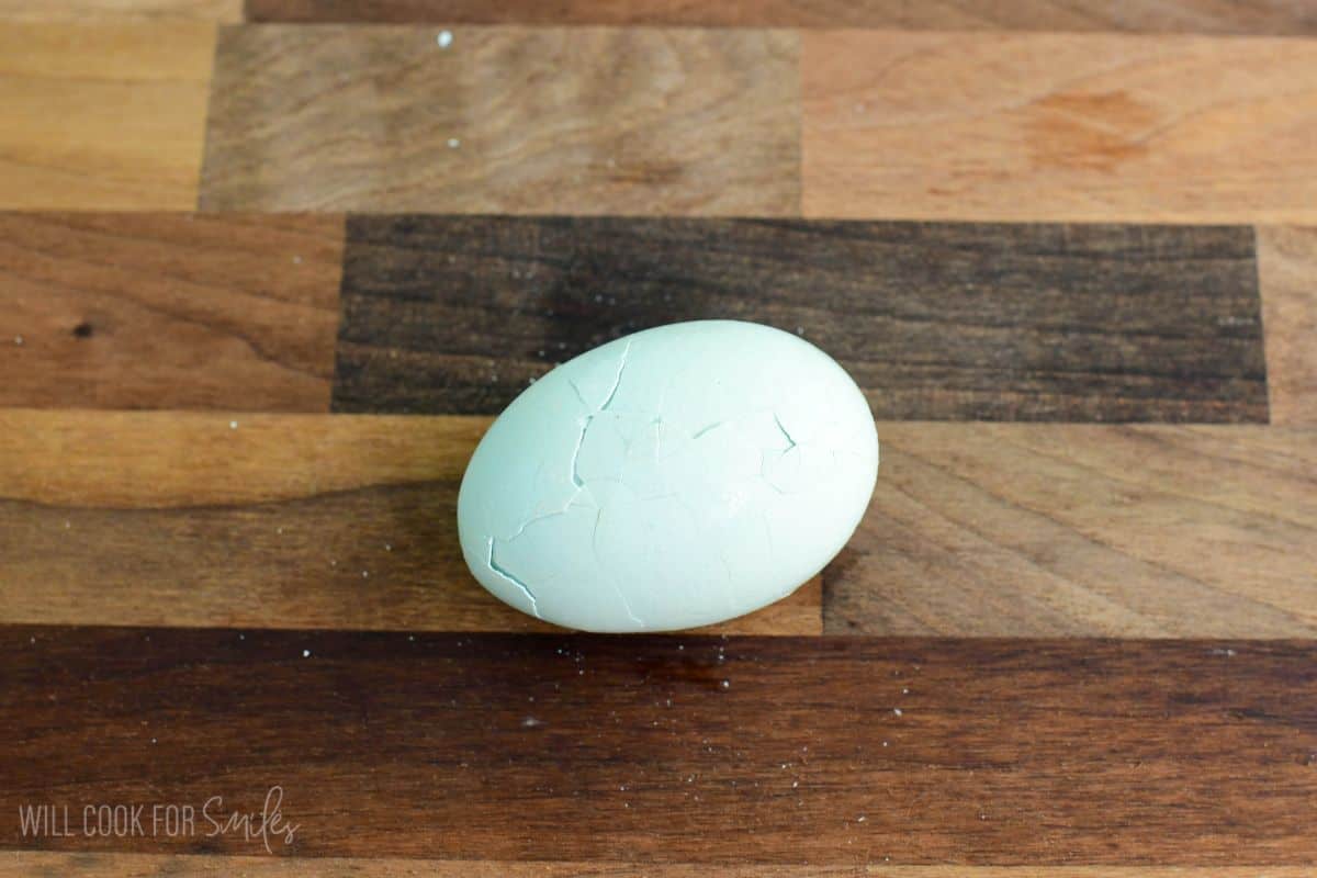Hard-boiled egg with a lightly cracked shell resting on a wooden cutting board.