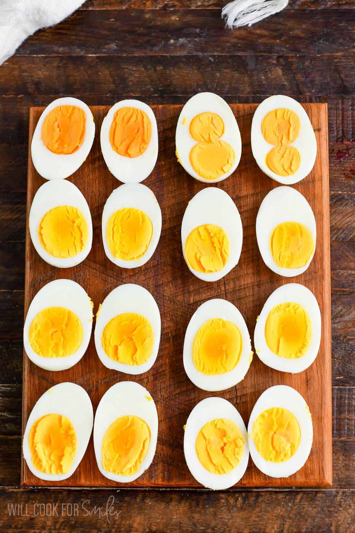a wooden board full of halved hard boiled eggs side by site.