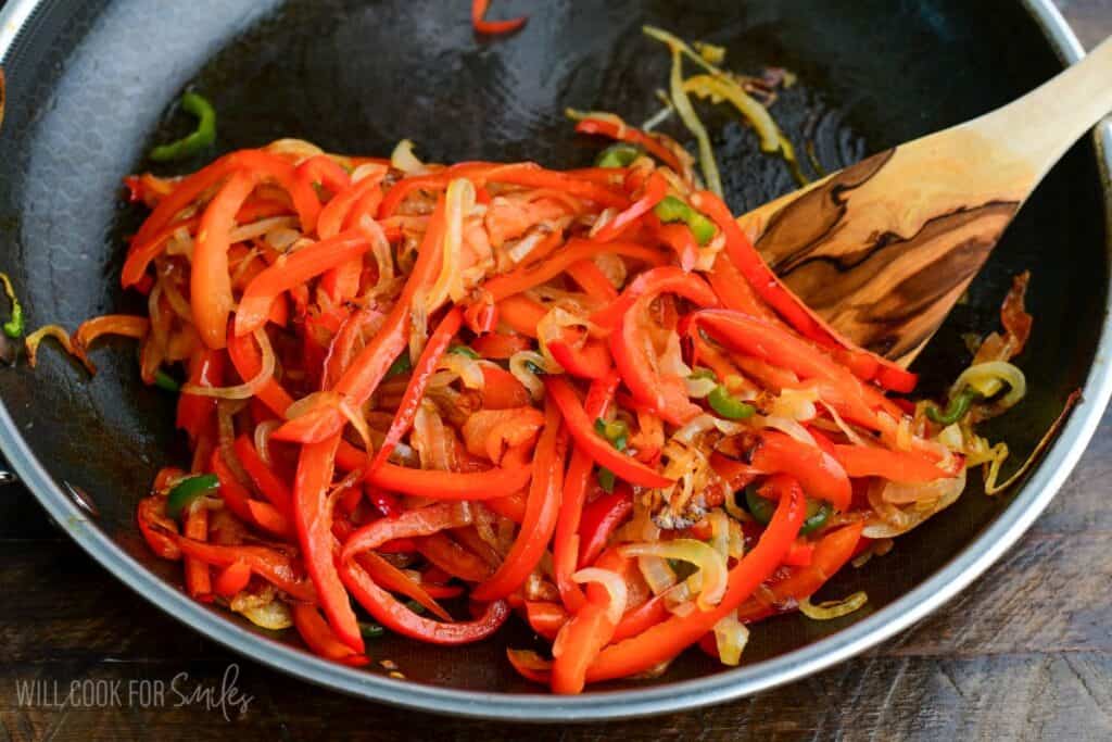 seared caramelized bell peppers, onions, and jalapenos in the cooking pan with wooden spoon.