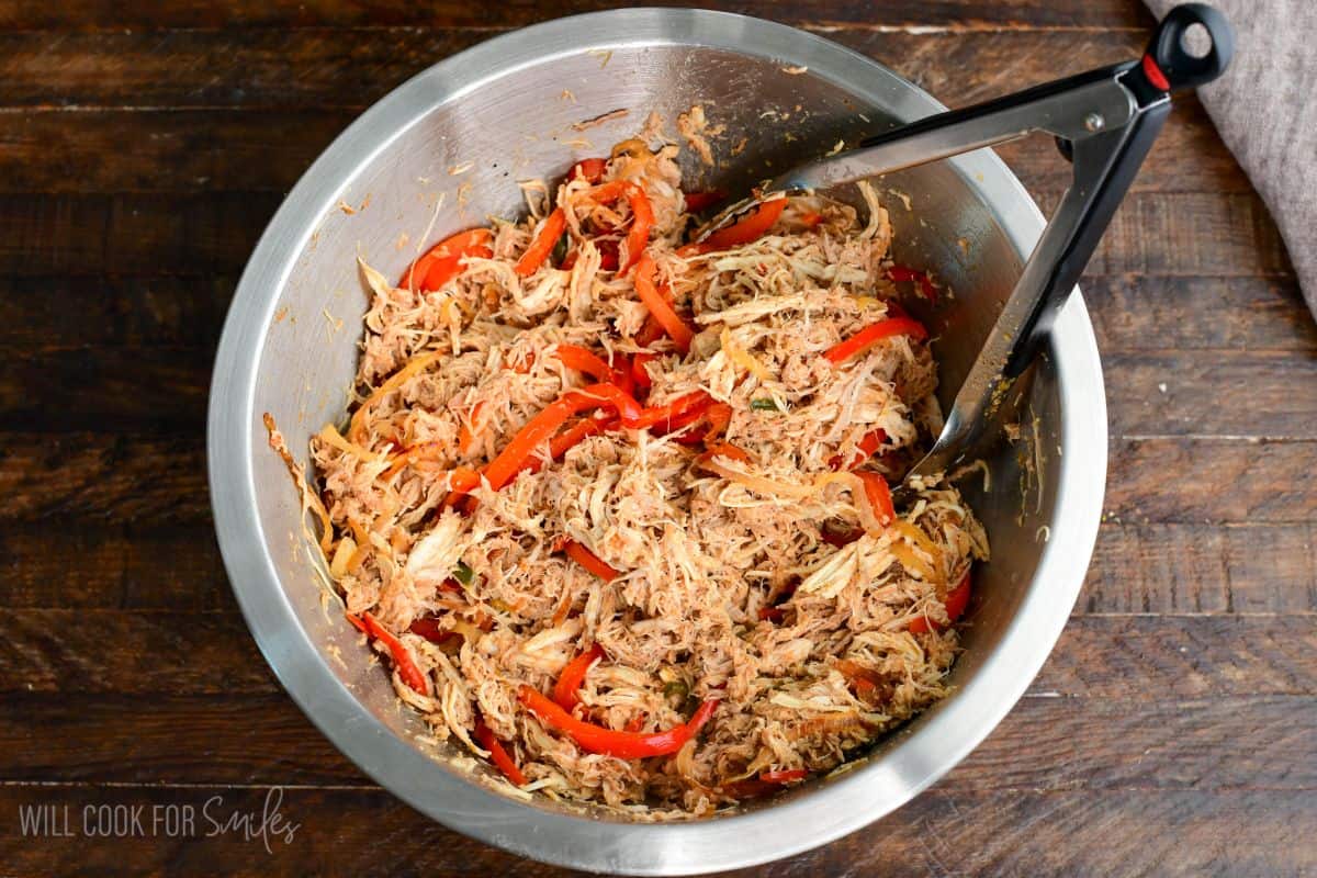 shredded moist and tender salsa chicken meat in the mixing bowl with sauteed vegetables mixed in.