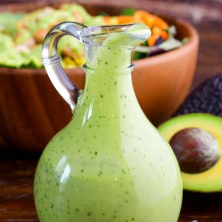 avocado dressing in a glass dressing bottle next to half an avocado and a salad.