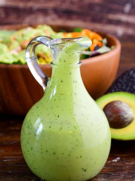 avocado dressing in a glass dressing bottle next to half an avocado and a salad.