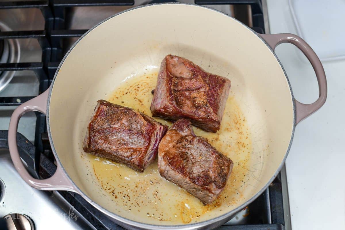 three short ribs searing in a Dutch oven.
