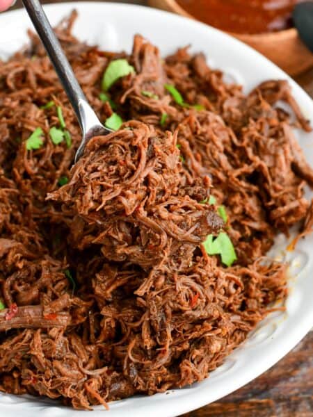 scooping out some tender shredded short ribs meat mixed with chili sauce out of a bowl.