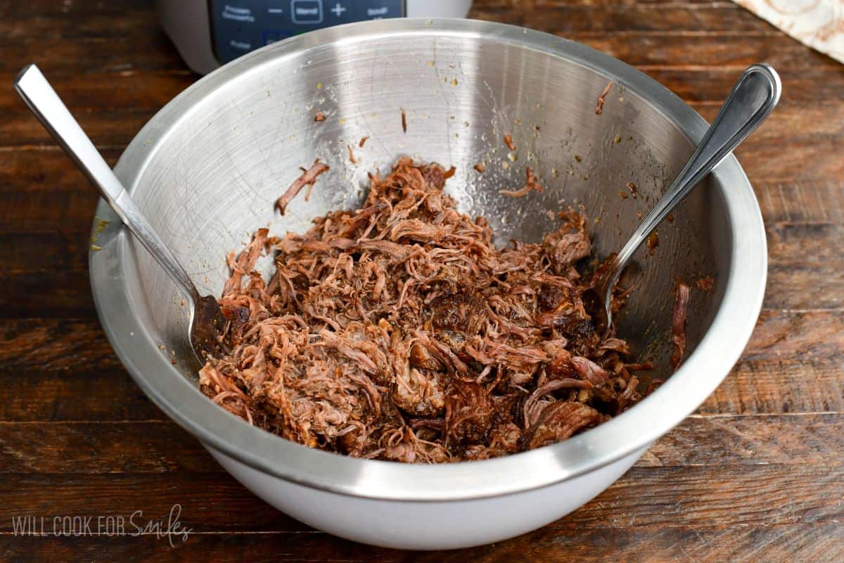 soft and tender shredded short rib meat in a mixing bowl with two forks.