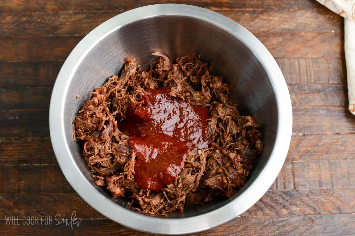 tender shredded beef short ribs in a mixing bowl with homemade chili sauce.