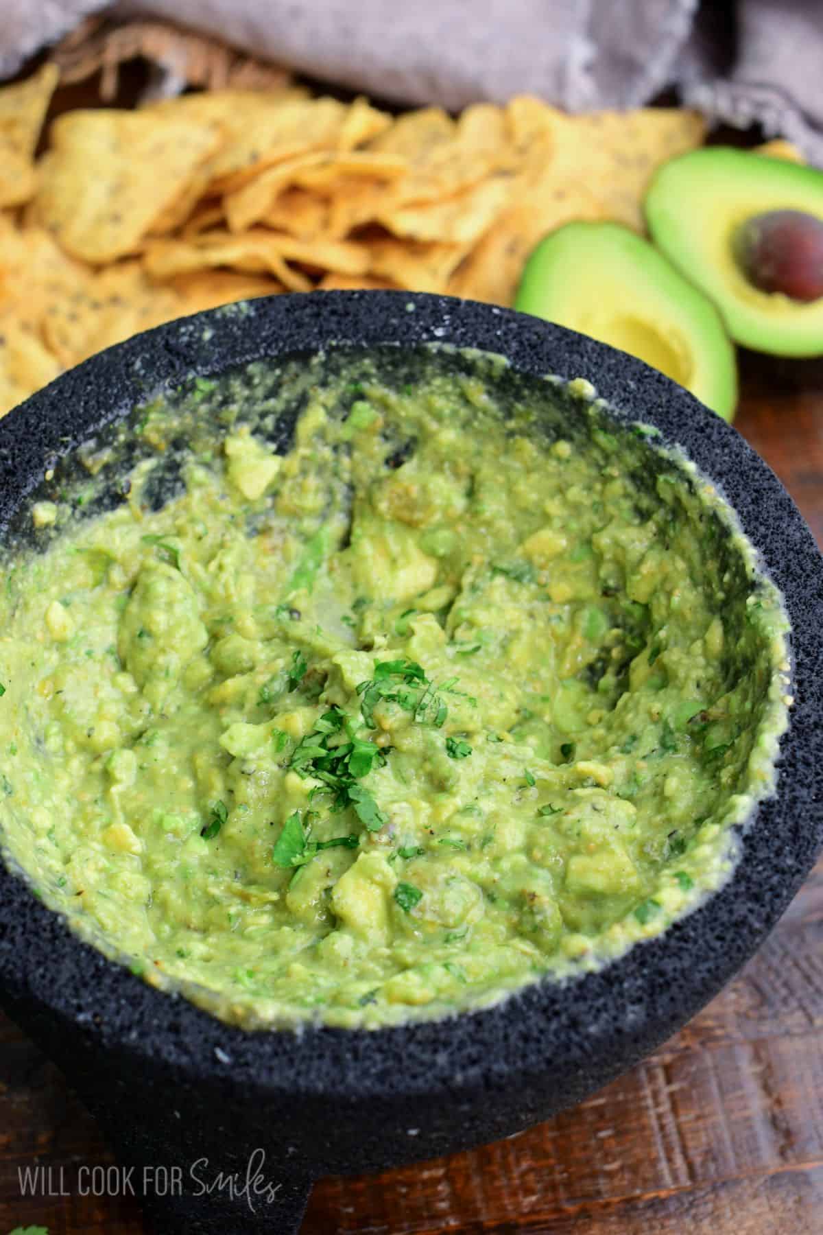 Oaxacan guacamole in a molcajete and chips and avocado behind it.
