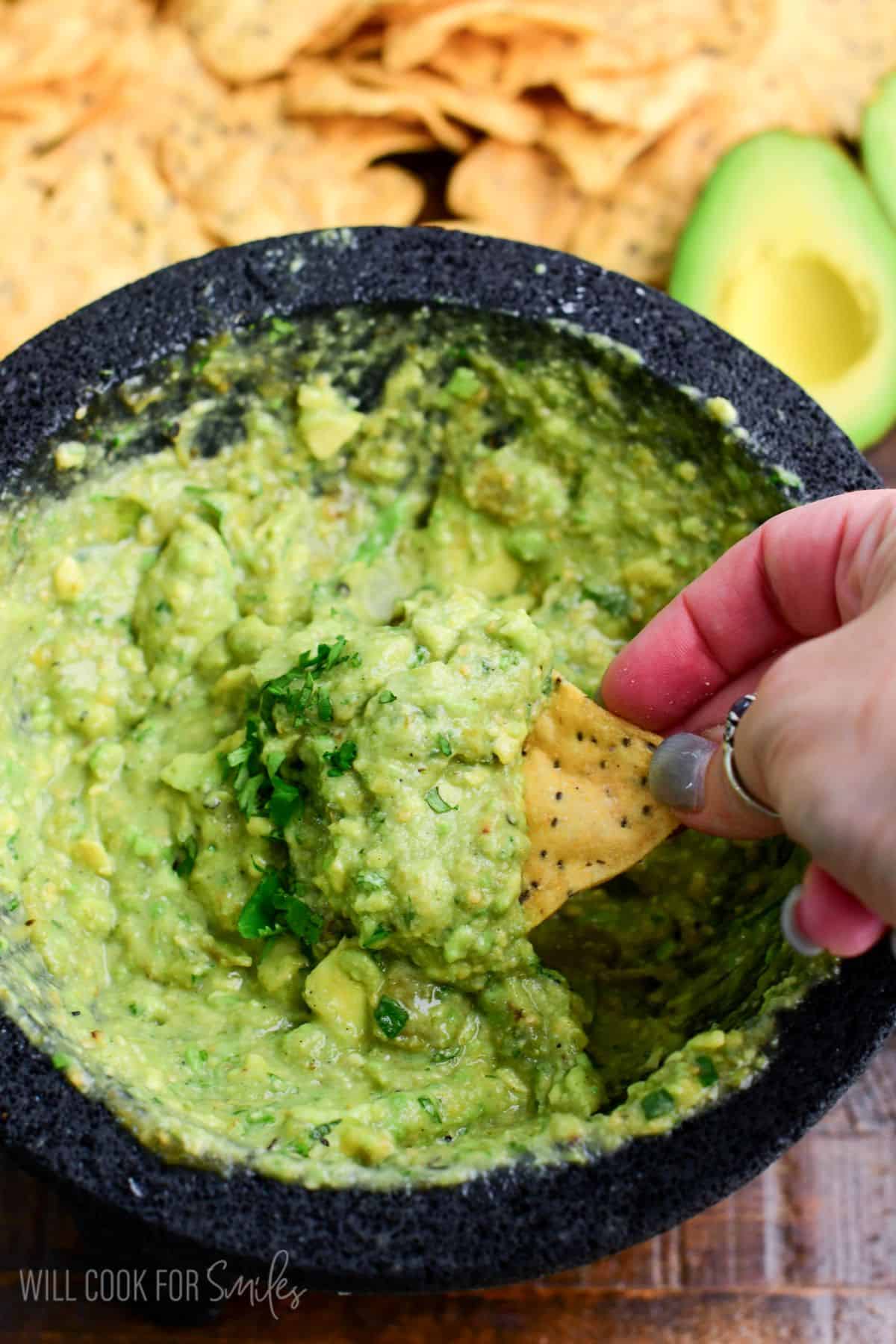 starting to scoop some Oaxacan guacamole from the molcajete bowl using a chip.