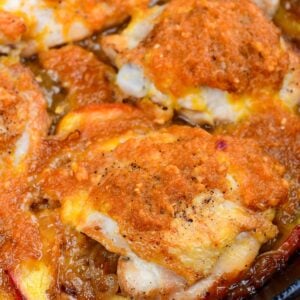 Close-up of baked peach chicken thighs in a skillet with fresh peaches and caramelized onion sauce.
