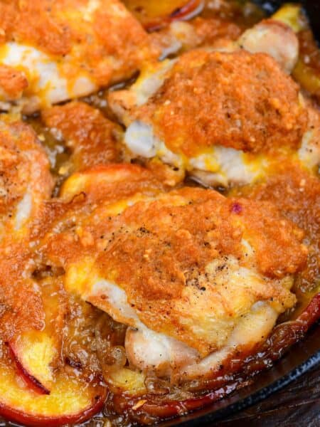 Close-up of baked peach chicken thighs in a skillet with fresh peaches and caramelized onion sauce.