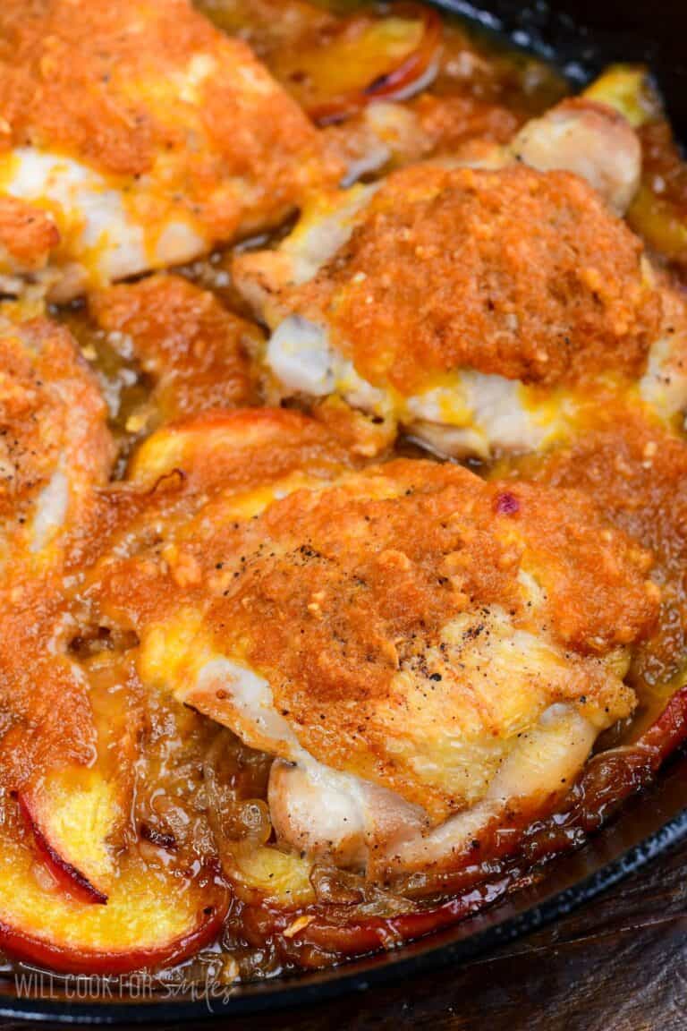 Close-up of baked peach chicken thighs in a skillet with fresh peaches and caramelized onion sauce.