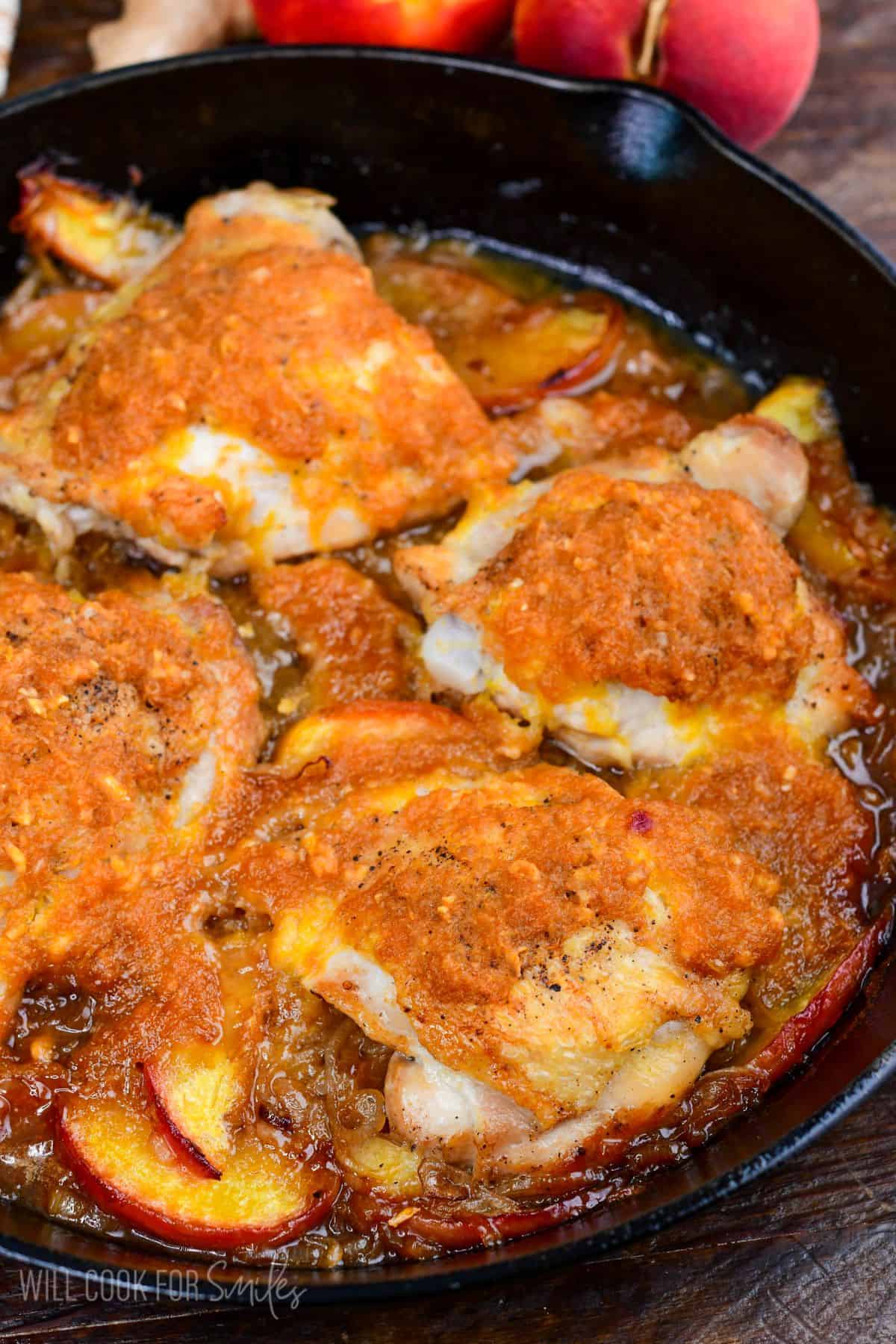Chicken thighs topped with peach sauce in a cast-iron skillet before baking with fresh peaches and onions.
