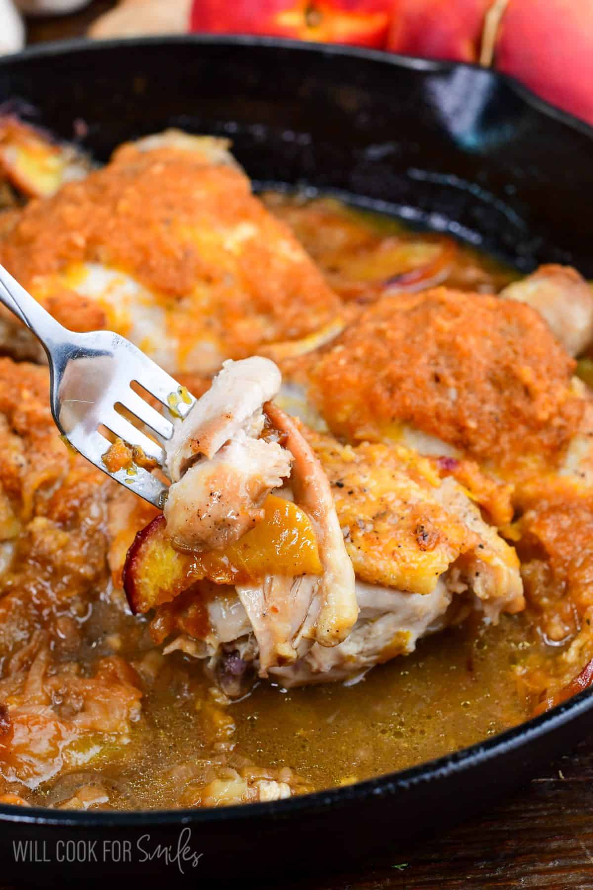 Fork holding juicy baked peach chicken with a tender bite, fresh peach, and savory peach onion sauce.