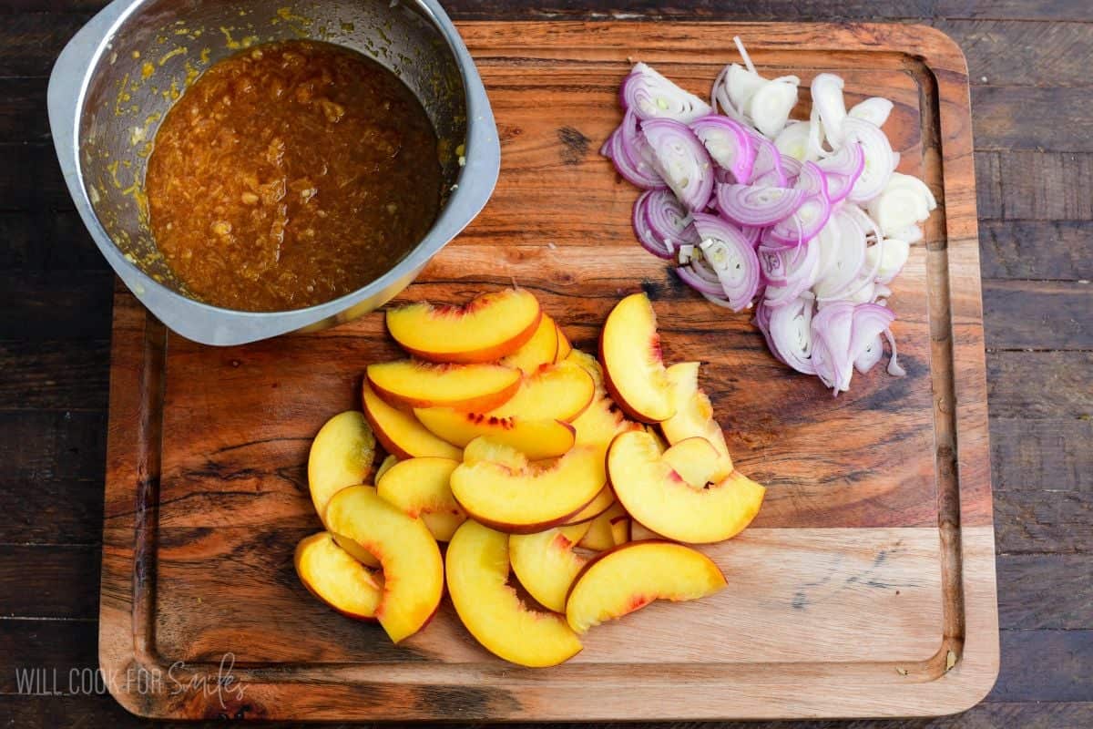 Sliced peaches, shallots, and peach sauce on a cutting board, ready to make baked peach chicken.