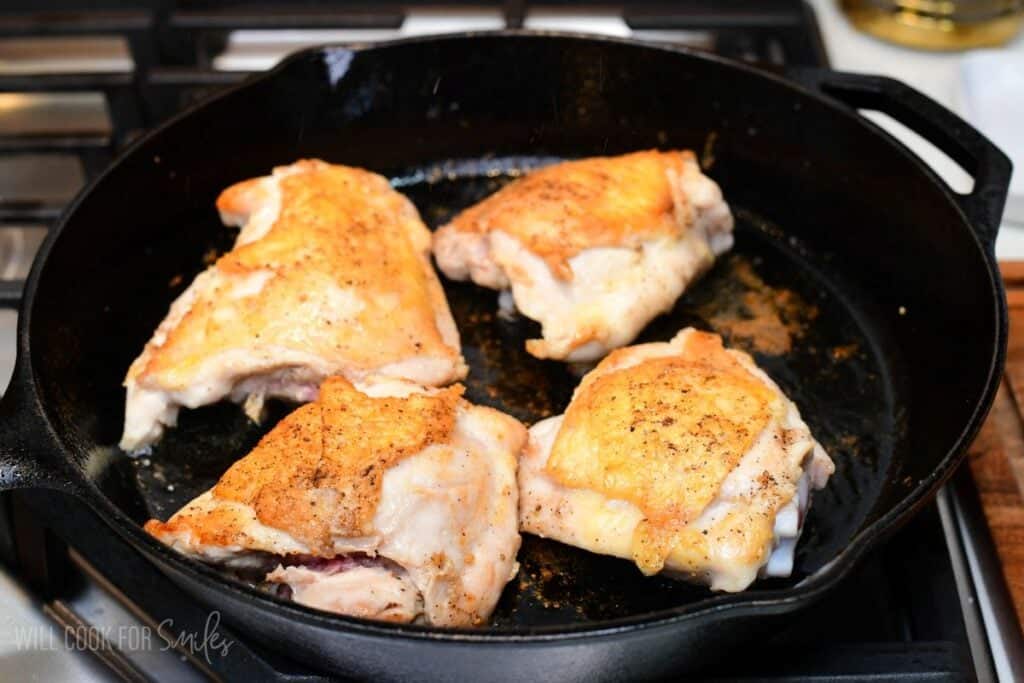 Chicken thighs searing skin-side down in a cast-iron skillet until the skin is crisp and golden brown.