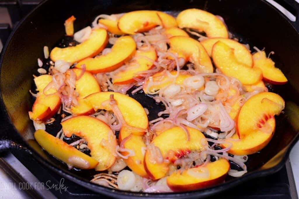 Fresh peaches and sliced shallots sautéing in a cast-iron skillet for baked peach chicken sauce.