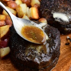 Spoon drizzling buttery pan juices over a coffee-rubbed filet mignon steak, served with roasted potatoes on a wooden platter.