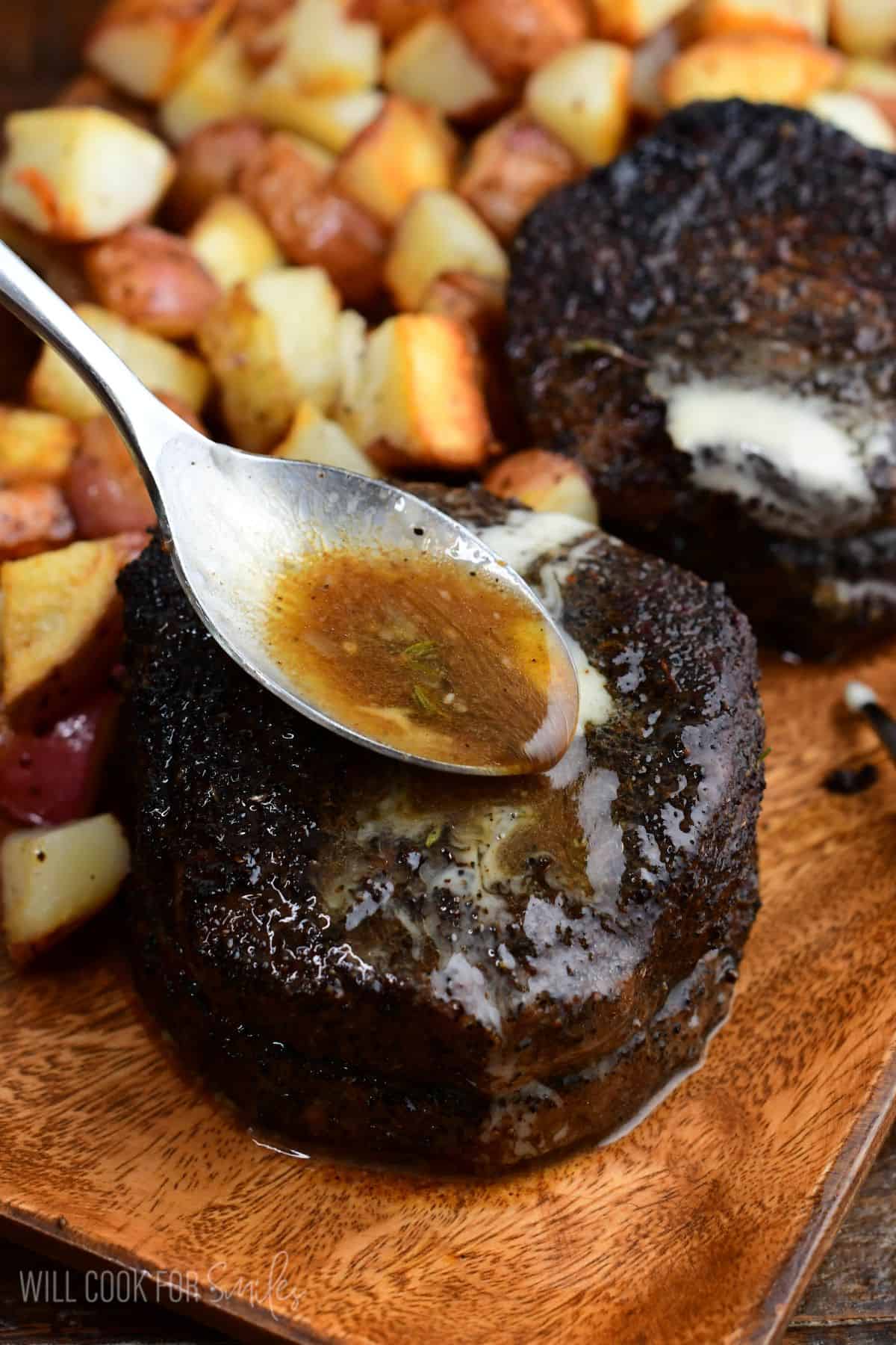 Spoon drizzling buttery pan juices over a coffee-rubbed filet mignon steak, served with roasted potatoes on a wooden platter.