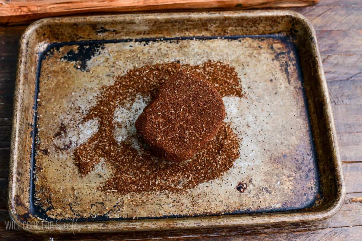 Filet mignon coated in coffee steak rub seasoning on a baking sheet, ready for cooking.