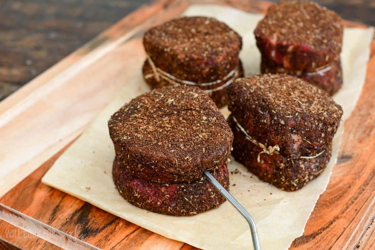 Coffee-rubbed filet mignon steaks resting on parchment paper, with a thermometer probe inserted into one steak to monitor cooking temperature.