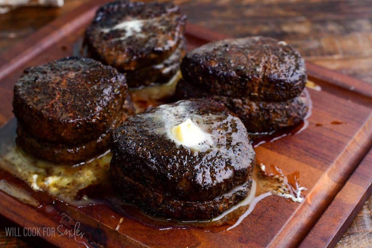 Coffee-rubbed filet mignon steaks resting on a wooden cutting board, topped with melting butter and pan juices after cooking.