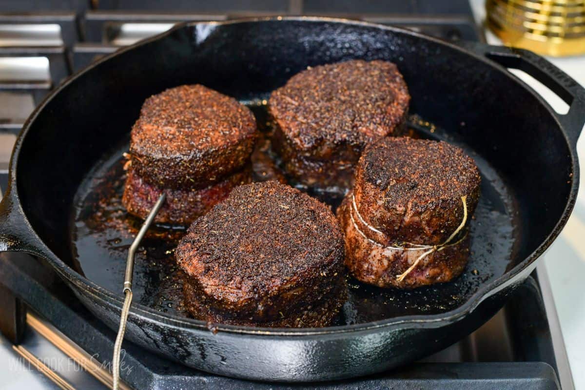 Coffee-rubbed filet mignon steaks on parchment paper, with a meat thermometer probe inserted into one steak to check the internal temperature before cooking.