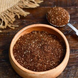Coffee steak rub seasoning blend in a wooden bowl with a measuring spoon filled with the spice mixture on a rustic wooden table.