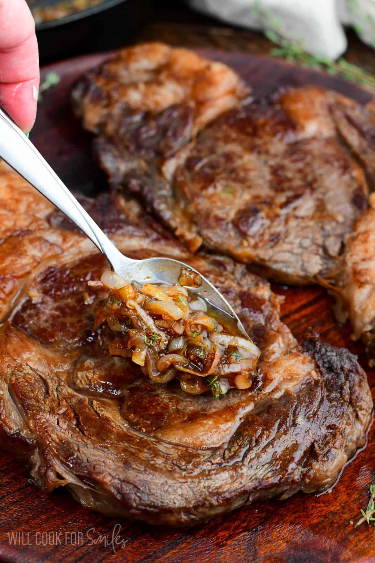 Spooning buttery shallot pan sauce over rested dry brined ribeye steaks on a wooden platter before serving.