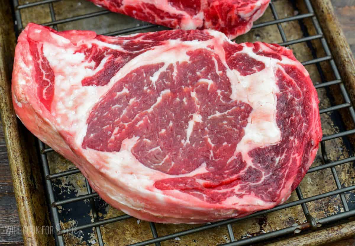 Dry brined ribeye steak resting on a wire rack after brining, showing marbling and a rich red color before cooking.