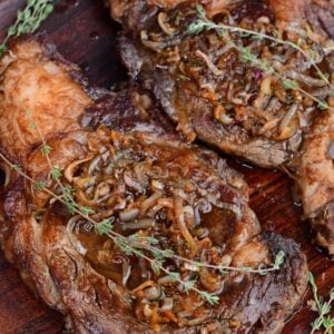 two juicy cooked dry brined ribeye steaks on a platter with caramelized onions and thyme on top.