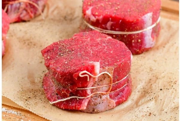 seasoned and tied filet magnon steak on parchment paper.