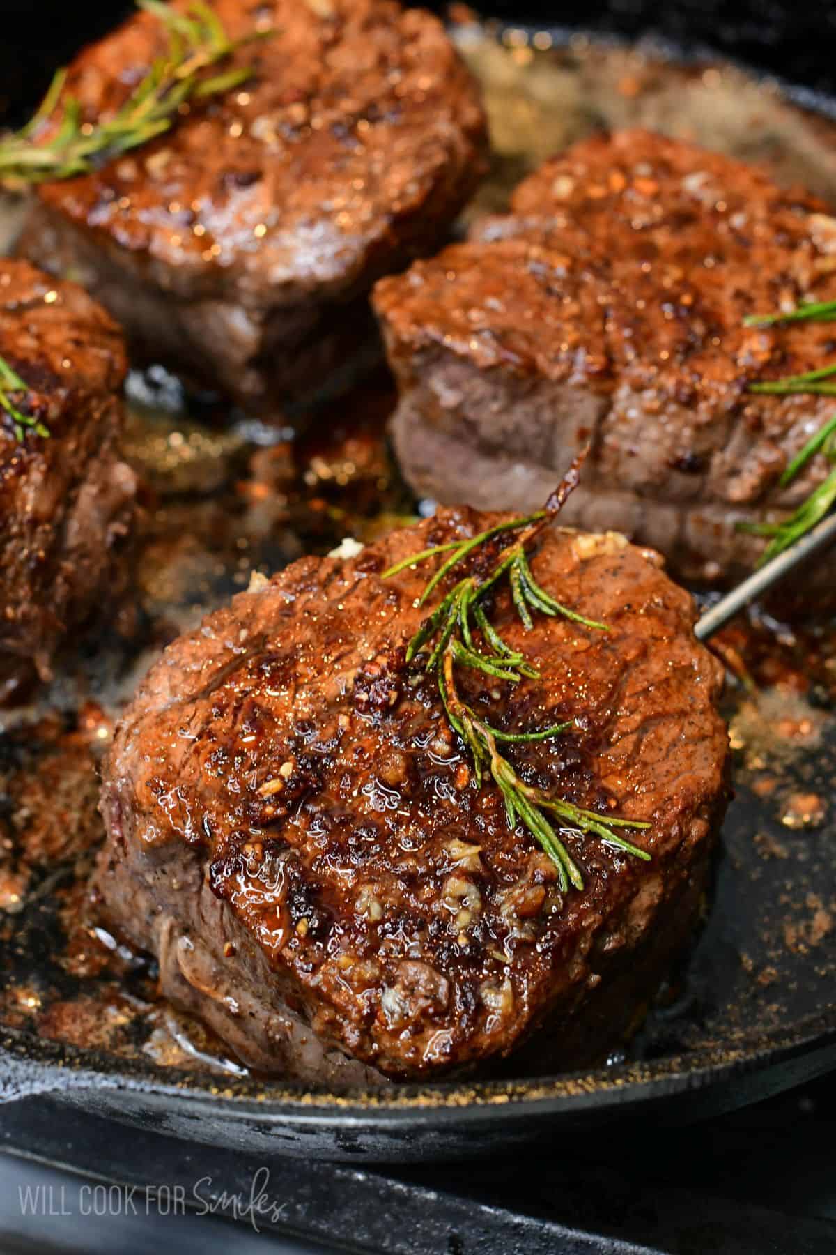 pan-seared filet mignon steaks cooking in a cast-iron skillet, coated in sizzling garlic-herb butter and topped with fresh rosemary sprigs.