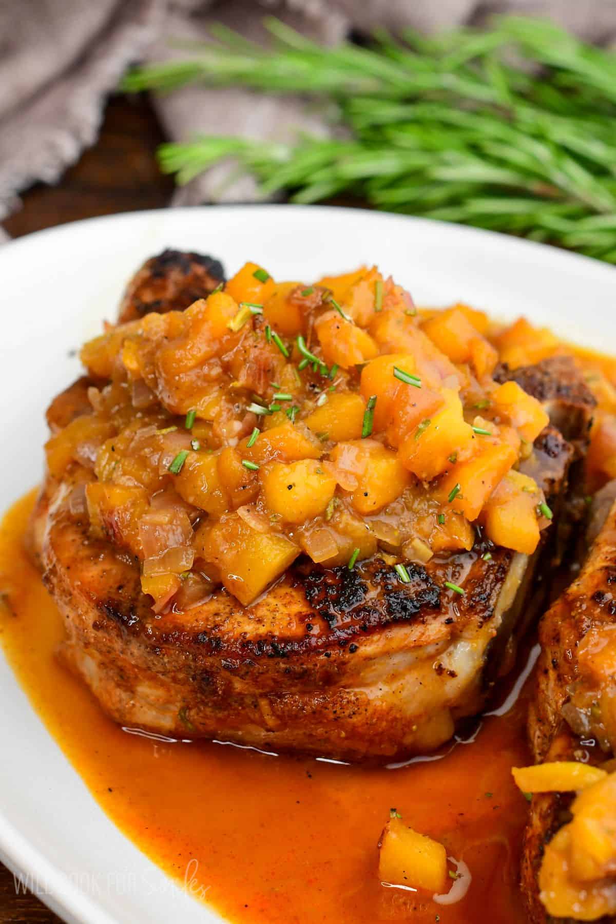 Peach pork chop topped with a chunky peach sauce, served on a plate with sweet and savory pan juices.