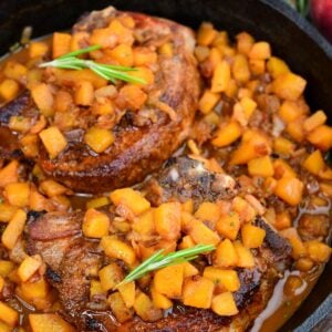 Peach pork chops simmered in a cast-iron skillet with diced peaches and savory peach sauce, garnished with rosemary.