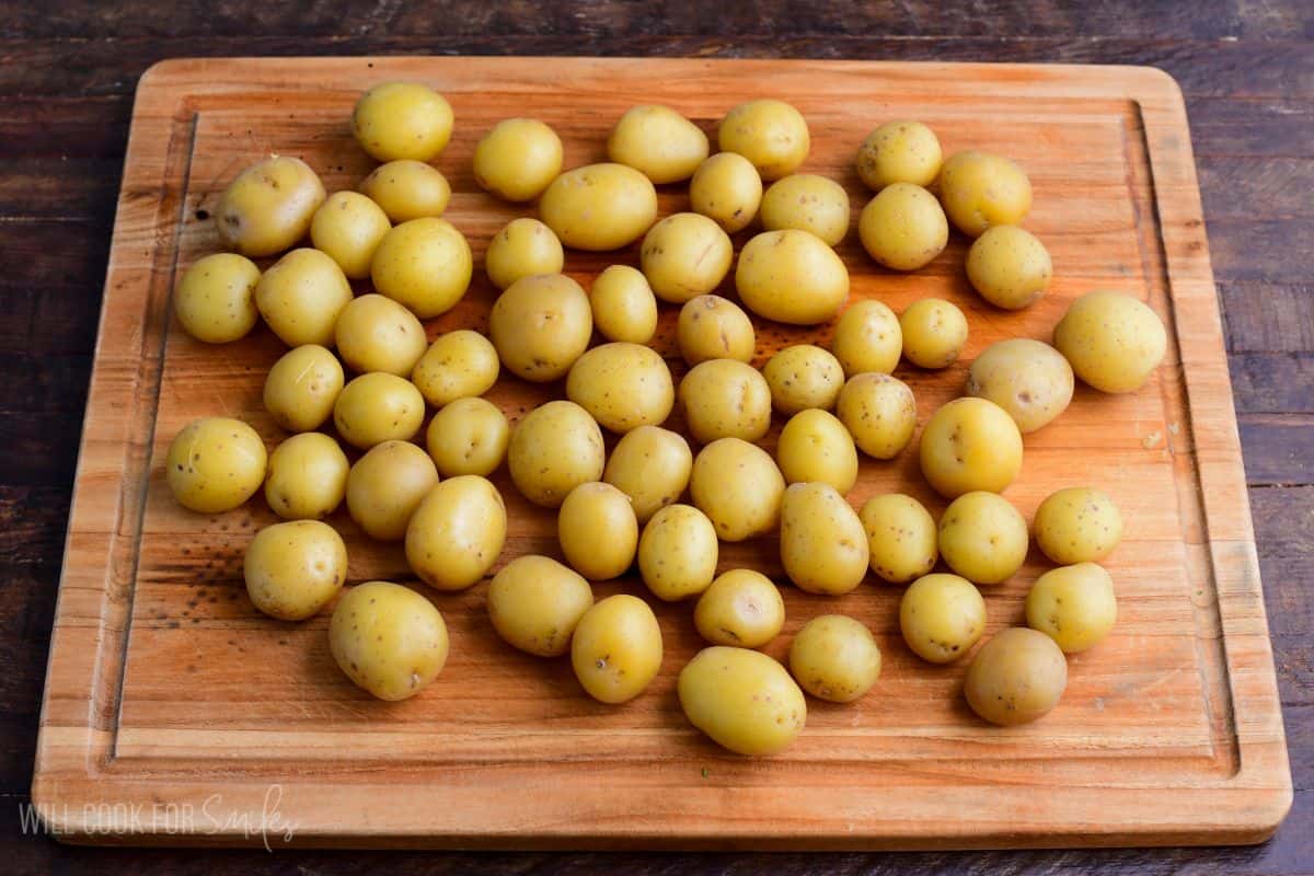 Cooked baby gold potatoes spread on a wooden cutting board, ready to cool before making potato salad.