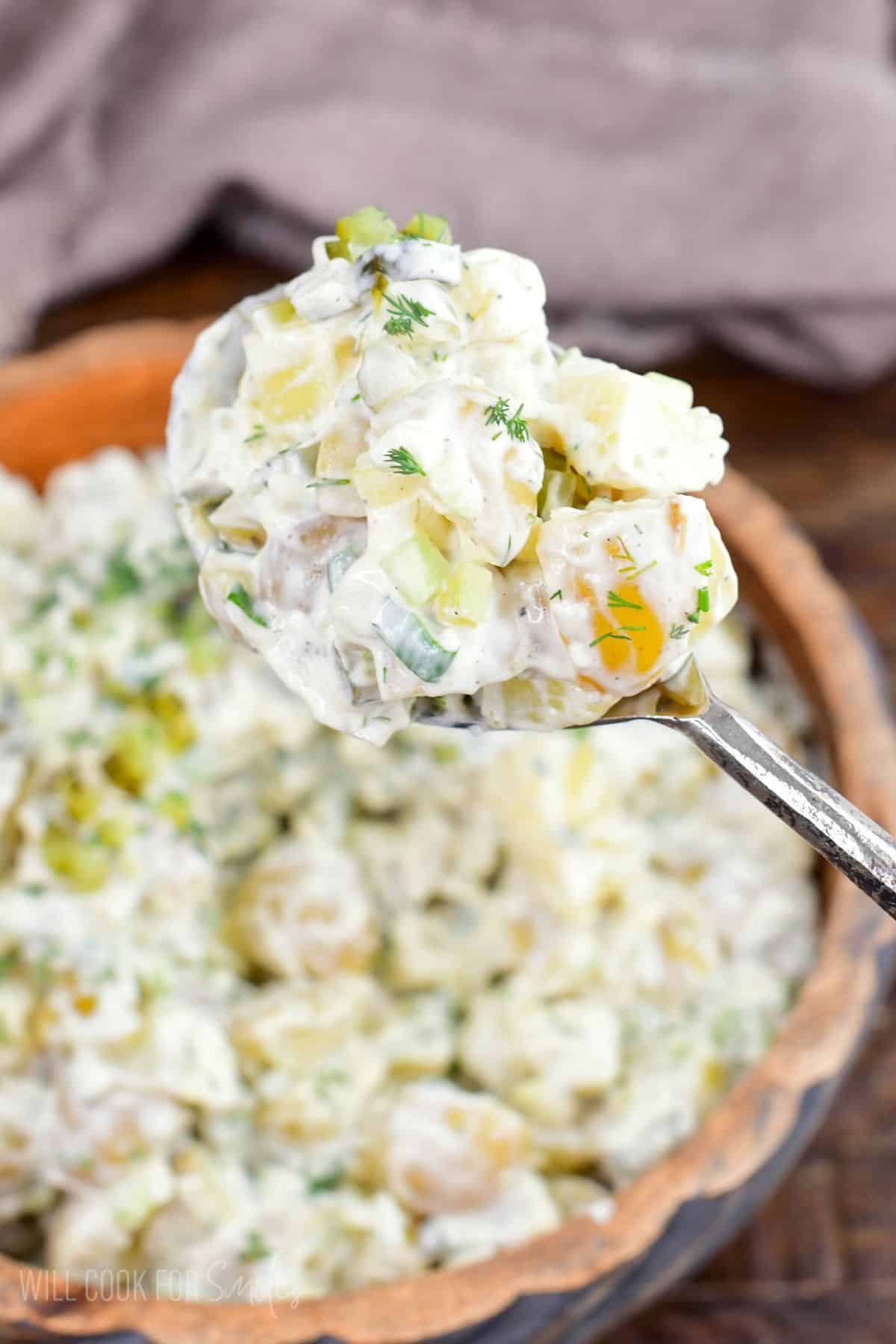 Spoonful of creamy dill pickle potato salad with tender potatoes, pickles, celery, eggs, and fresh dill.