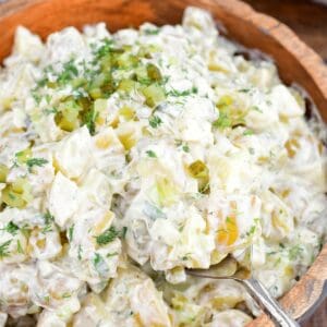 Creamy dill pickle potato salad in a wooden bowl with potatoes, eggs, celery, pickles, and fresh dill.