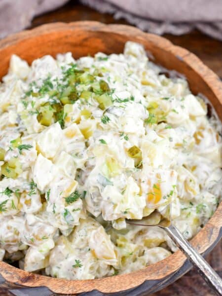 Creamy dill pickle potato salad in a wooden bowl with potatoes, eggs, celery, pickles, and fresh dill.