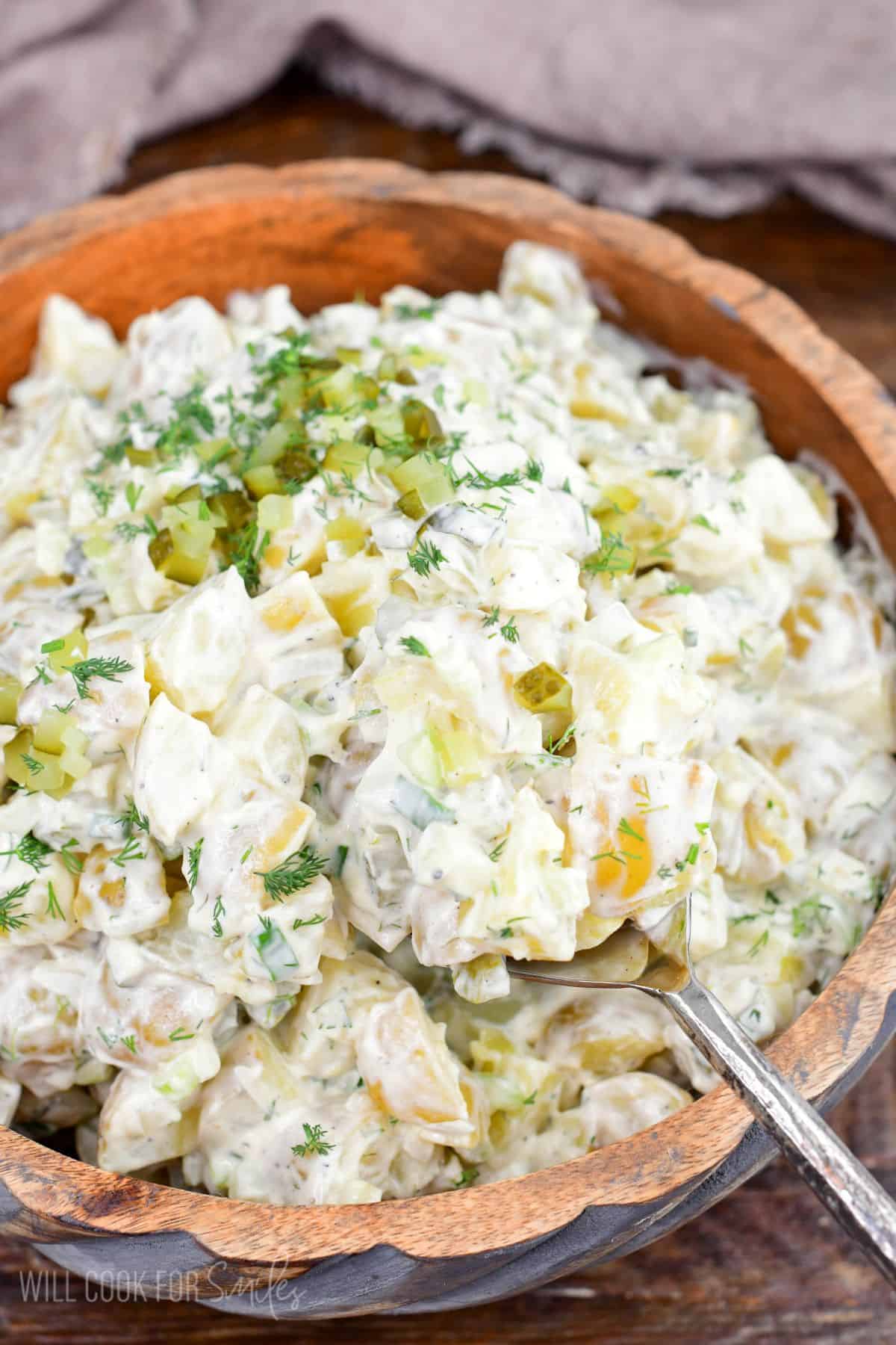 Creamy dill pickle potato salad in a wooden bowl with potatoes, eggs, celery, pickles, and fresh dill.