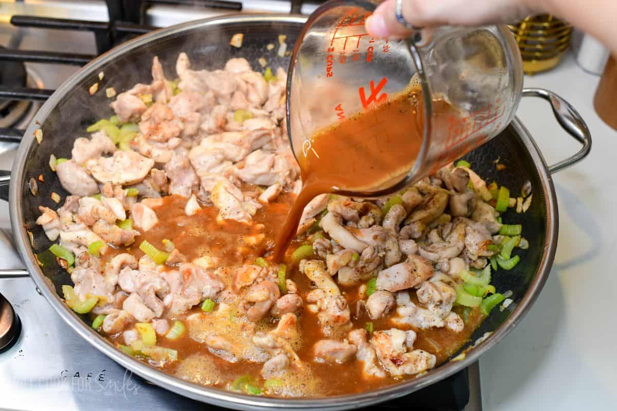 Pouring pepper sauce over browned chicken, celery, and onion in a skillet.