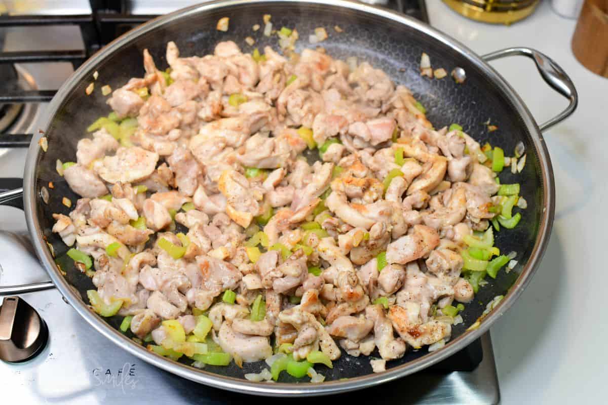 Browned chicken cooking with tender celery and onion in a skillet for pepper chicken.