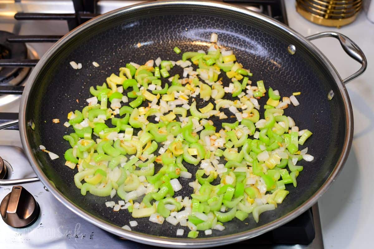 Celery and onion sautéing in a skillet until tender and lightly browned for pepper chicken.