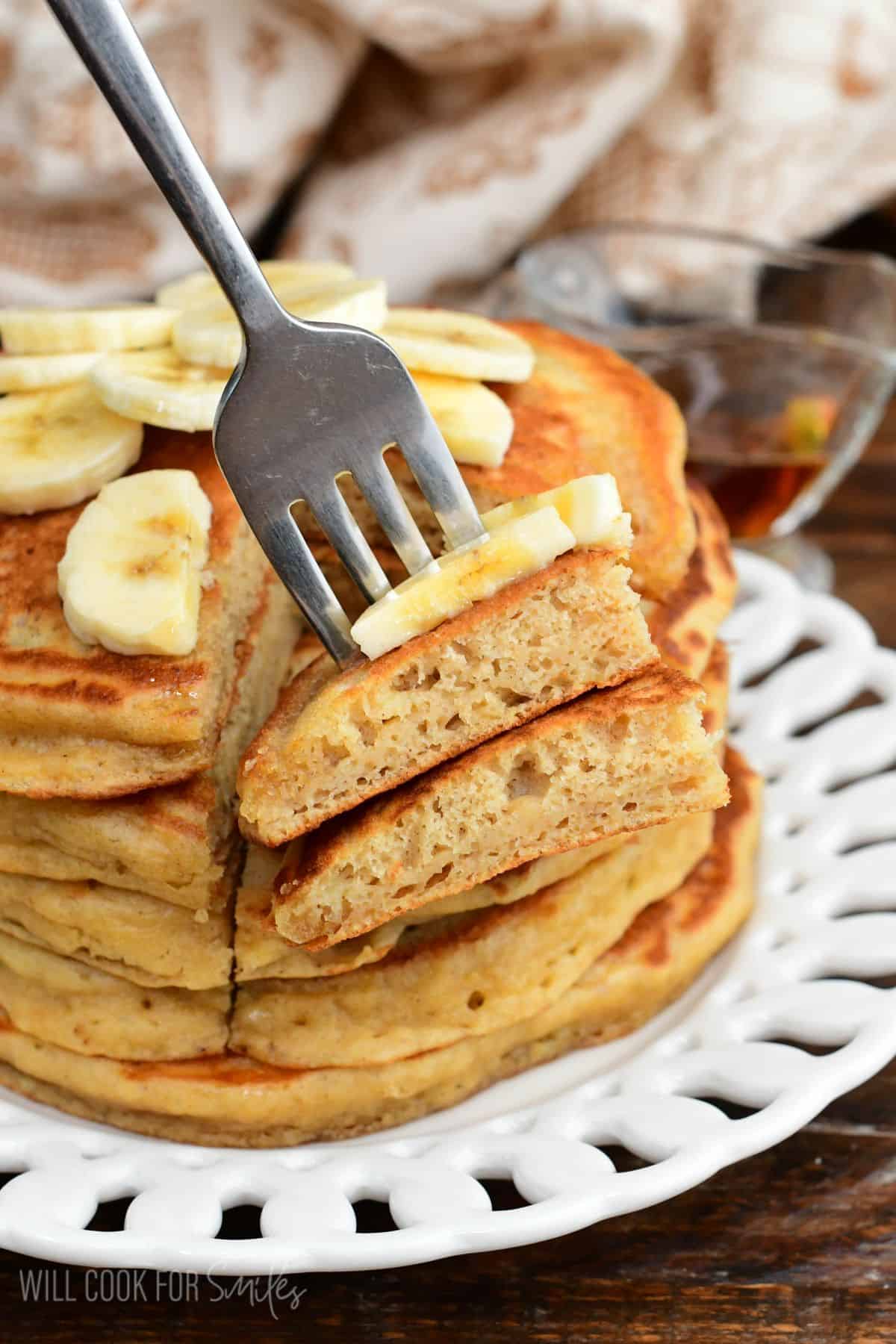 Stack of fluffy banana pancakes cut open to show the soft center, topped with banana slices and served with syrup.
