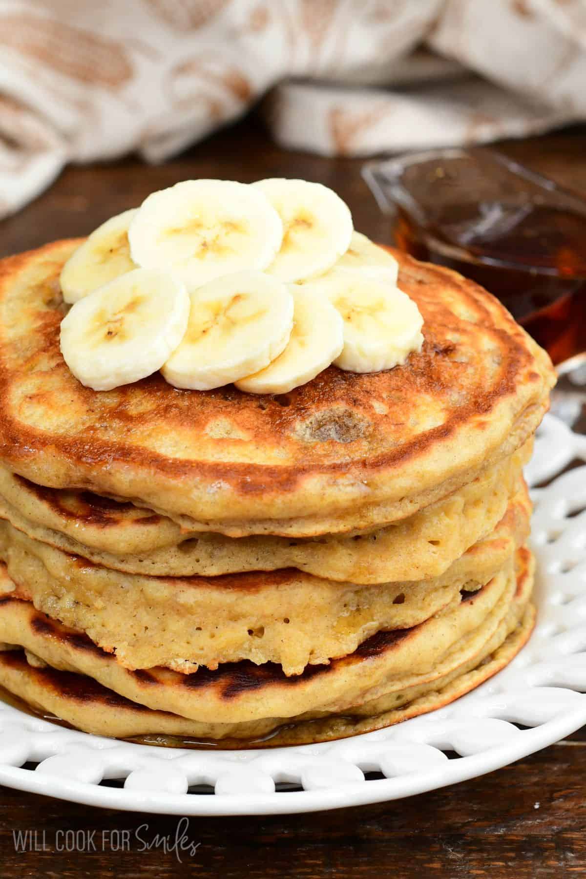 Stack of fluffy banana pancakes topped with fresh banana slices, served with maple syrup on the side.