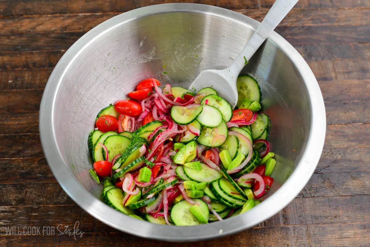Cucumber tomato onion salad with fresh vegetables and herbs tossed together in a large mixing bowl.